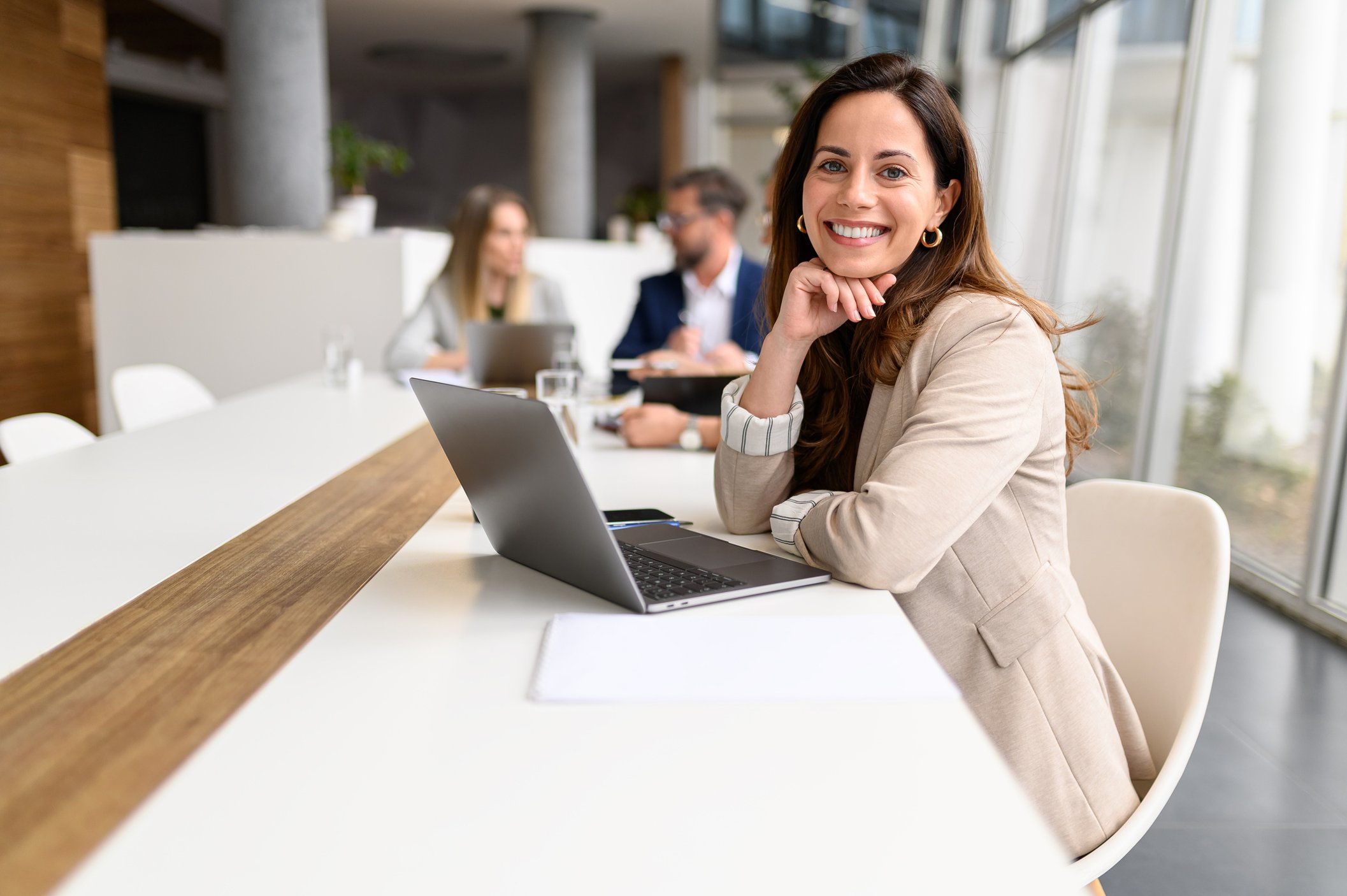 Person sat at a desk with an open laptop. They are turned towards the camera smiling.